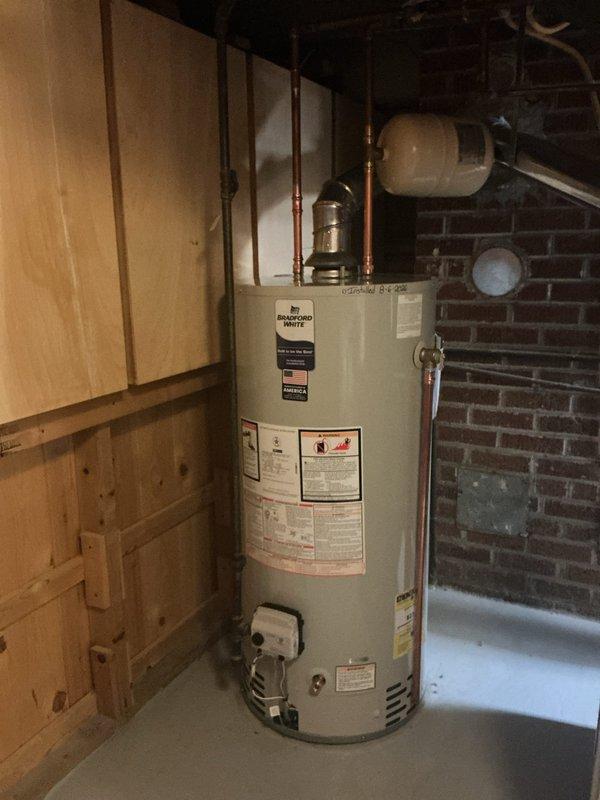 Removed existing Bradford White residential water heater and installed new replacement unit in basement utility area. Installation included all necessary copper piping connections to integrate with existing plumbing system. Added thermal expansion tank to bring installation into compliance with current plumbing code requirements. New water heater includes 6-year manufacturer warranty and was installed against exposed brick wall with proper clearances maintained. All connections pressure-tested and verified operational upon completion.