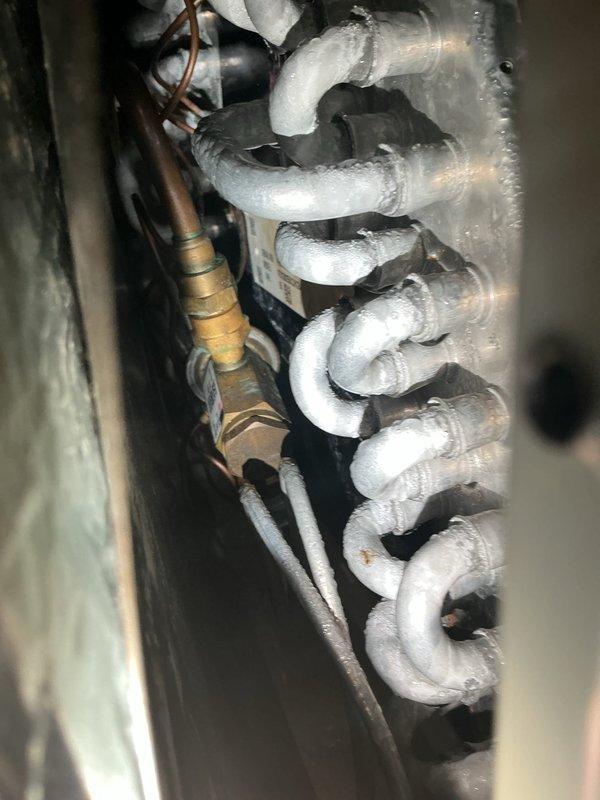 Performed maintenance visit on 12-year-old air conditioning system. Upon inspection, discovered evaporator coil completely frozen with heavy ice buildup throughout the serpentine coil assembly. Conducted electrical diagnostics using clamp meter, recording amperage draw of 7.53 amps at the system components. Documented frost accumulation on coil and refrigerant lines with photographic evidence for service records.