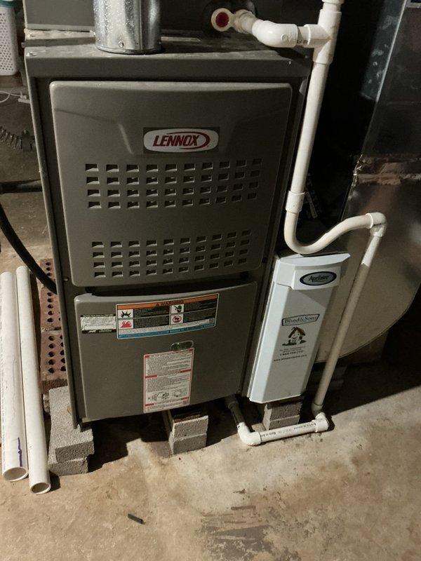 Completed preventive maintenance cooling visit on 4-year-old Lennox HVAC system. Performed comprehensive system inspection including visual examination of furnace cabinet, air handler components, and condensate drainage system. Accessed and inspected air filtration system through hinged access panel, verifying pleated filter condition and proper installation within white metal frame. Checked PVC condensate drain lines for proper operation and drainage flow. Inspected manufacturer specification plates and verified all safety labels present and legible. Examined unit mounting on concrete base and surrounding area for any signs of water damage or system leakage. All components found operating within normal parameters with no immediate service concerns identified. System ready for continued cooling operation.