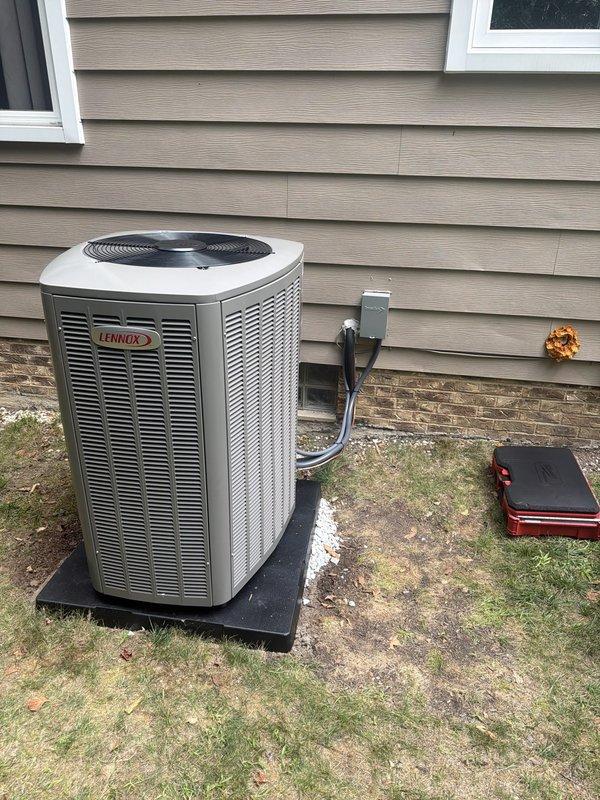 Completed full HVAC system installation including an 80% efficiency Lennox furnace, Lennox air conditioning condenser unit, and humidifier. The outdoor condenser was positioned on a black equipment pad against the exterior wall with proper electrical disconnect and refrigerant line connections routed through the wall. Inside the basement mechanical room, installed the new Lennox furnace with complete ductwork assembly and integrated the humidifier into the system. All equipment was properly connected, tested for operation, and left in full working condition.