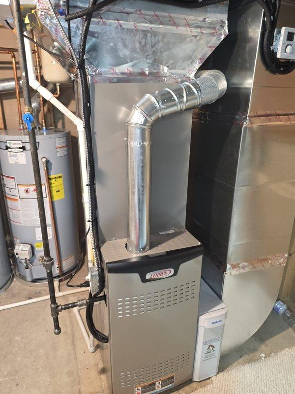 Completed full HVAC system installation including an 80% efficiency Lennox furnace, Lennox air conditioning condenser unit, and humidifier. The outdoor condenser was positioned on a black equipment pad against the exterior wall with proper electrical disconnect and refrigerant line connections routed through the wall. Inside the basement mechanical room, installed the new Lennox furnace with complete ductwork assembly and integrated the humidifier into the system. All equipment was properly connected, tested for operation, and left in full working condition.