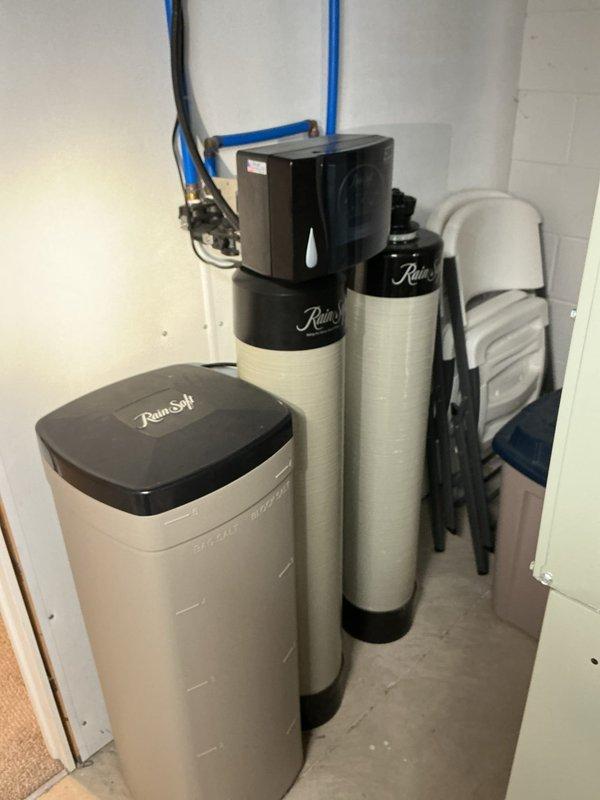 Responded to service call for toilet leaking from bottom seal. Upon arrival, inspected toilet and surrounding plumbing infrastructure including main line access points. Evaluated water treatment system and drainage piping for potential main line obstruction that could contribute to leaking issue. Documented existing plumbing conditions including PVC drain lines showing age-related discoloration and water treatment equipment installation for comprehensive assessment of overall system performance.