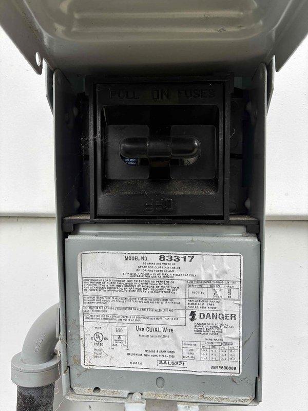 Performed scheduled maintenance visit on 10-year-old residential air conditioning system. Inspected electrical disconnect box and verified proper operation of safety disconnect switch. Checked manufacturer specifications on unit nameplate (Model No. 83317). Conducted electrical diagnostics using digital clamp meter, measuring voltage and amperage at the outdoor unit. Recorded readings of 0.09 and 49.29 on meter display while testing electrical components. Inspected control board wiring connections and verified all wire terminations were secure. Documented equipment condition with photos for maintenance records. System operational upon completion of inspection.
