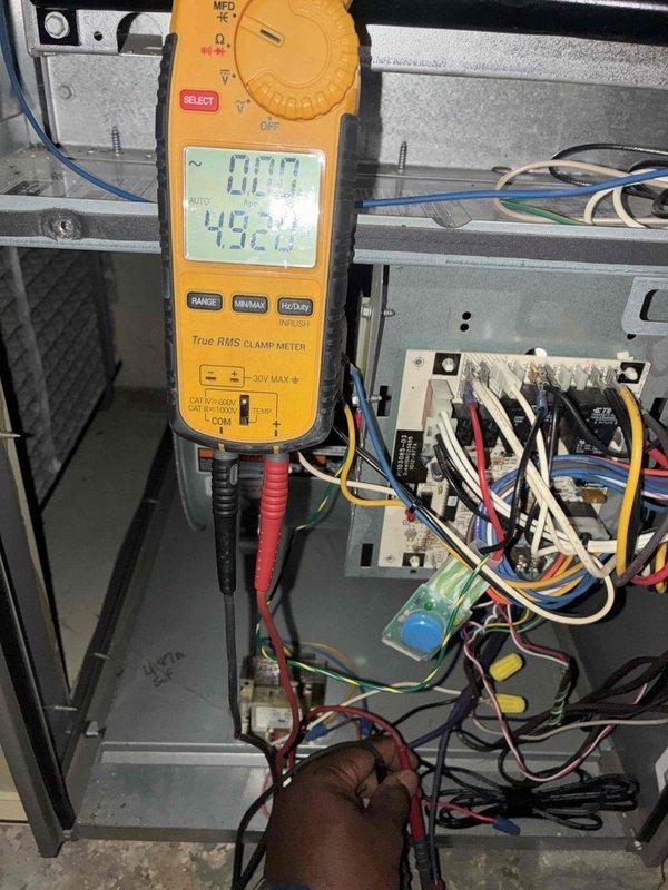 Performed scheduled maintenance visit on 10-year-old residential air conditioning system. Inspected electrical disconnect box and verified proper operation of safety disconnect switch. Checked manufacturer specifications on unit nameplate (Model No. 83317). Conducted electrical diagnostics using digital clamp meter, measuring voltage and amperage at the outdoor unit. Recorded readings of 0.09 and 49.29 on meter display while testing electrical components. Inspected control board wiring connections and verified all wire terminations were secure. Documented equipment condition with photos for maintenance records. System operational upon completion of inspection.