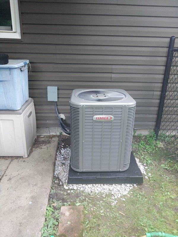 Completed installation of Lennox air conditioning system with matching evaporator coil at residential property. Positioned outdoor condenser unit on composite pad with white gravel base against exterior wall with gray horizontal siding. Installed electrical disconnect box on siding and ran conduit from disconnect to unit per code requirements. Ensured proper clearances around equipment for adequate airflow and future service access. System installed as second AC unit for property, tested and confirmed operational upon completion.
