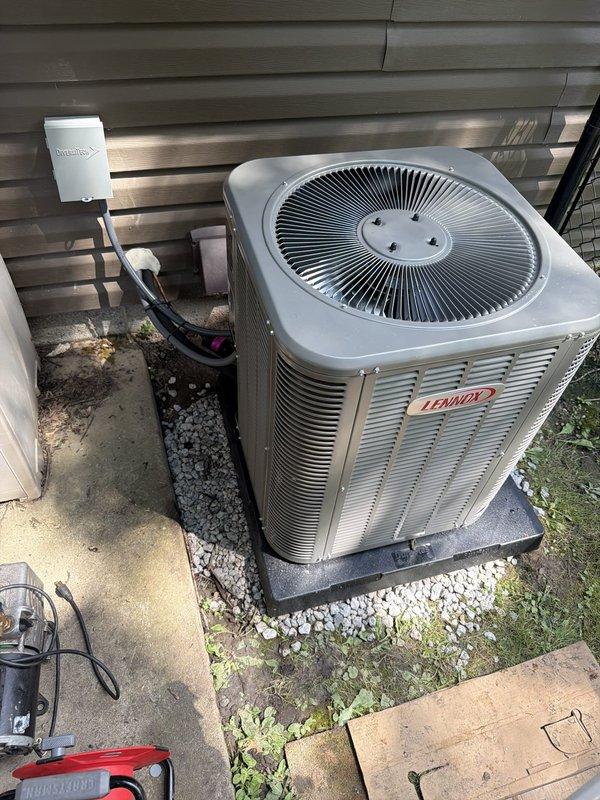 Completed installation of Lennox air conditioning system with matching evaporator coil at residential property. Positioned outdoor condenser unit on composite pad with white gravel base against exterior wall with gray horizontal siding. Installed electrical disconnect box on siding and ran conduit from disconnect to unit per code requirements. Ensured proper clearances around equipment for adequate airflow and future service access. System installed as second AC unit for property, tested and confirmed operational upon completion.
