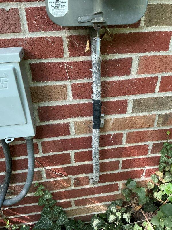 Conducted inspection of exterior electrical service entrance following customer report of deteriorated entrance cable. Documented compromised metal conduit with visible damage and improper repairs including electrical tape wrapping on sections of the service mast. Photographed weathered electrical meter box, junction panel connections, and affected conduit routing along brick exterior wall for assessment and future replacement planning.