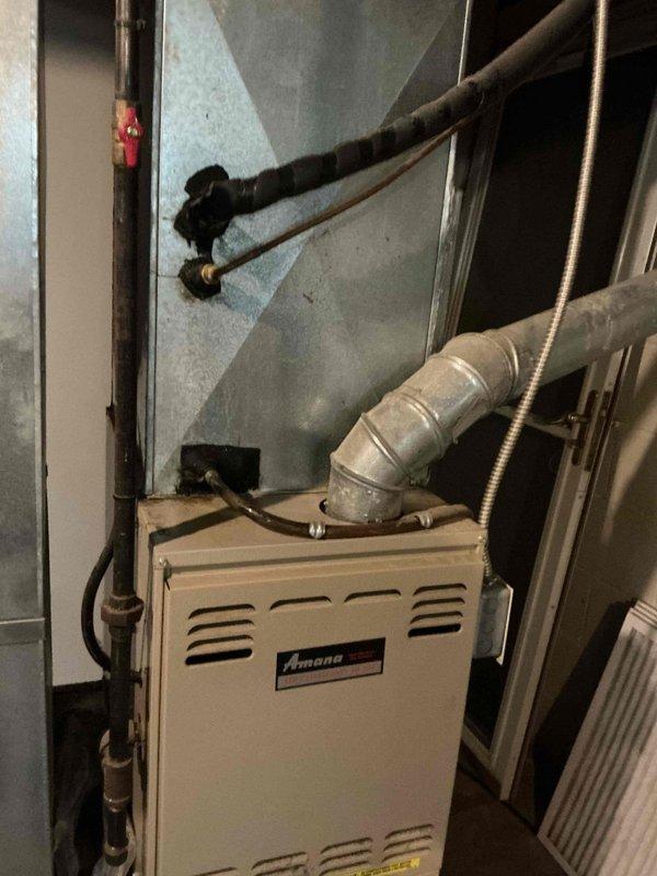 Responded to service call for loud groaning noise occurring when blower motor engages on 24-year-old air conditioning system with 28-year-old Amana furnace. Upon arrival, performed diagnostic inspection of the HVAC system located in utility closet. Examined furnace unit, blower assembly, ductwork connections, and associated mechanical components. Documented existing equipment condition including aged furnace with standard wear patterns consistent with equipment age. Assessed metallic ductwork, flexible ducting connections, and pipe routing for potential noise sources. Given the advanced age of both the air conditioning and furnace systems, identified blower motor bearings or motor mount as likely cause of groaning noise during fan operation, though further operational testing during cooling cycle would be required for definitive diagnosis.
