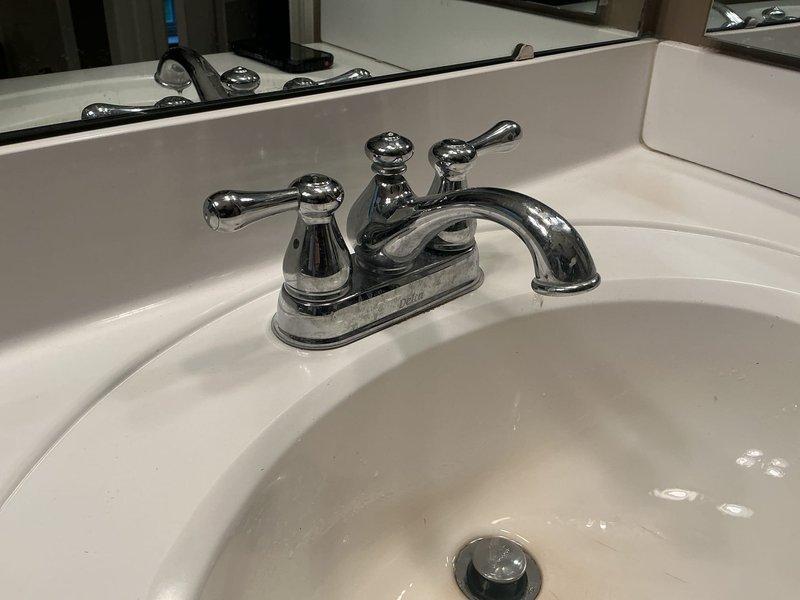 Responded to service call for two faucet repairs in residential bathroom, with one unit experiencing significant dripping. Inspected chrome two-handle centerset faucet assembly on white porcelain sink and diagnosed worn internal components causing leak. Disassembled faucet handles, replaced deteriorated cartridges and O-rings, reassembled unit, and tested for proper operation and seal integrity. Verified elimination of drip and restored full functionality to both handles with appropriate water flow and temperature control.