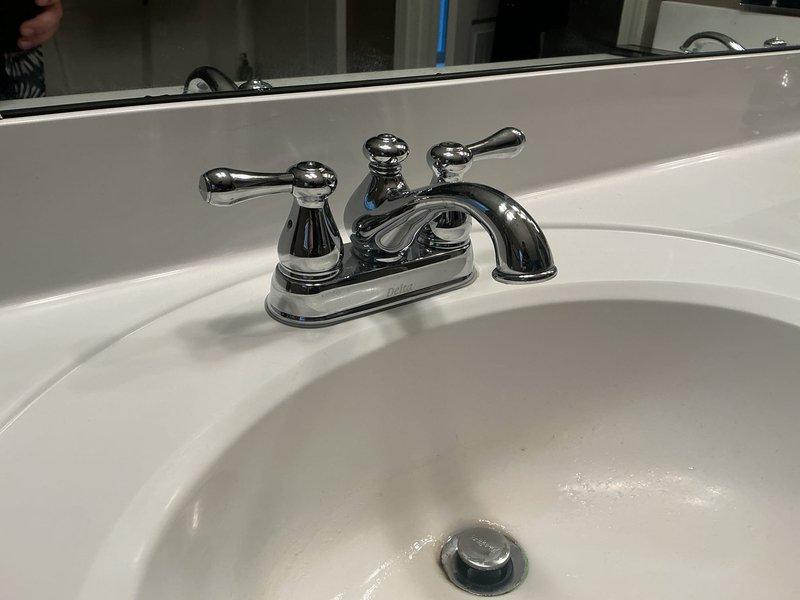 Responded to service call for two faucet repairs in residential bathroom, with one unit experiencing significant dripping. Inspected chrome two-handle centerset faucet assembly on white porcelain sink and diagnosed worn internal components causing leak. Disassembled faucet handles, replaced deteriorated cartridges and O-rings, reassembled unit, and tested for proper operation and seal integrity. Verified elimination of drip and restored full functionality to both handles with appropriate water flow and temperature control.