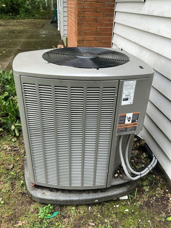 Responded to service call for 9-year-old Lennox central air conditioning system that had been physically displaced 8-10 inches by fallen tree branch and was no longer producing cold air. Upon arrival, found condenser unit sitting unlevel on concrete pad with potential damage from impact. Inspected refrigerant lines and confirmed both suction and liquid lines were ambient temperature, indicating loss of refrigeration cycle. Assessed unit positioning, checked for visible damage to cabinet, coil fins, and refrigerant line connections. Documented current condition of displaced unit with photographs showing unit against house exterior with visible offset from original position. System requires releveling, complete refrigerant leak check, potential line set inspection for kinks or damage, and full operational assessment once unit is properly repositioned and secured.