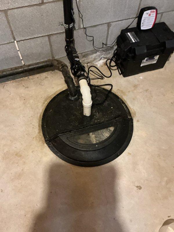 Installed battery backup system for existing sump pump to ensure continuous operation during power outages. The installation included mounting the backup battery unit adjacent to the sump basin, connecting the power supply and control wiring to the primary pump system, and integrating the discharge piping with the existing vertical PVC assembly that routes to the exterior drainage system.