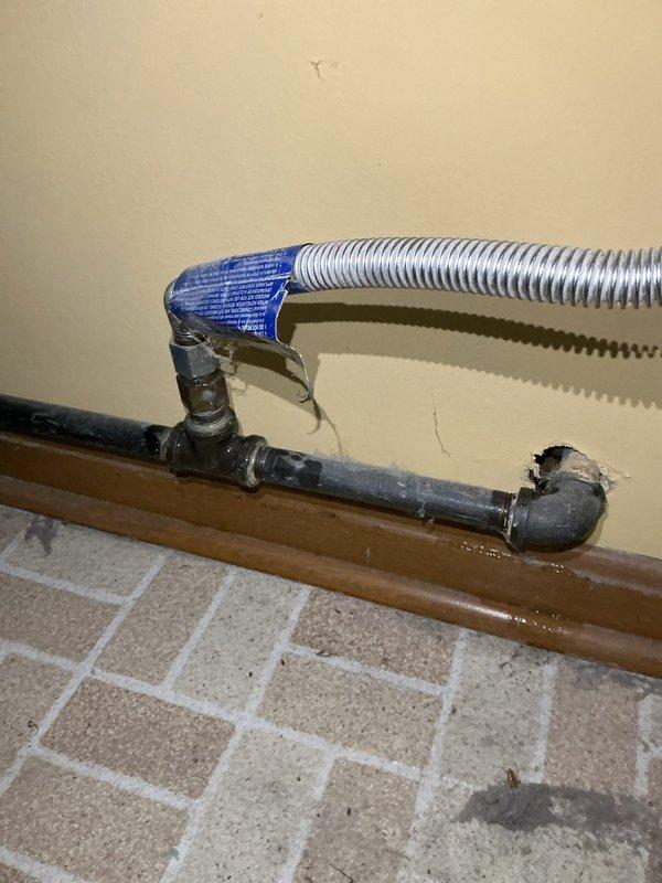 Responded to emergency natural gas leak at residential property. Located active gas leak at damaged baseboard piping connection where copper gas line enters through wall at floor level. Shut off gas supply at valve to eliminate safety hazard. Assessed existing piping configuration including corrugated flexible connector with compromised fitting and evidence of water damage to surrounding baseboard and wall structure. Secured leak point and verified gas flow cessation. Prepared area for proper gas line repair to enable safe dryer hookup that previous contractor was unable to complete due to leak condition.