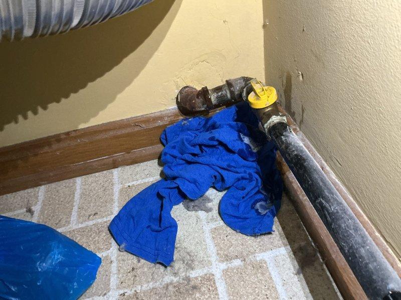 Responded to emergency natural gas leak at residential property. Located active gas leak at damaged baseboard piping connection where copper gas line enters through wall at floor level. Shut off gas supply at valve to eliminate safety hazard. Assessed existing piping configuration including corrugated flexible connector with compromised fitting and evidence of water damage to surrounding baseboard and wall structure. Secured leak point and verified gas flow cessation. Prepared area for proper gas line repair to enable safe dryer hookup that previous contractor was unable to complete due to leak condition.
