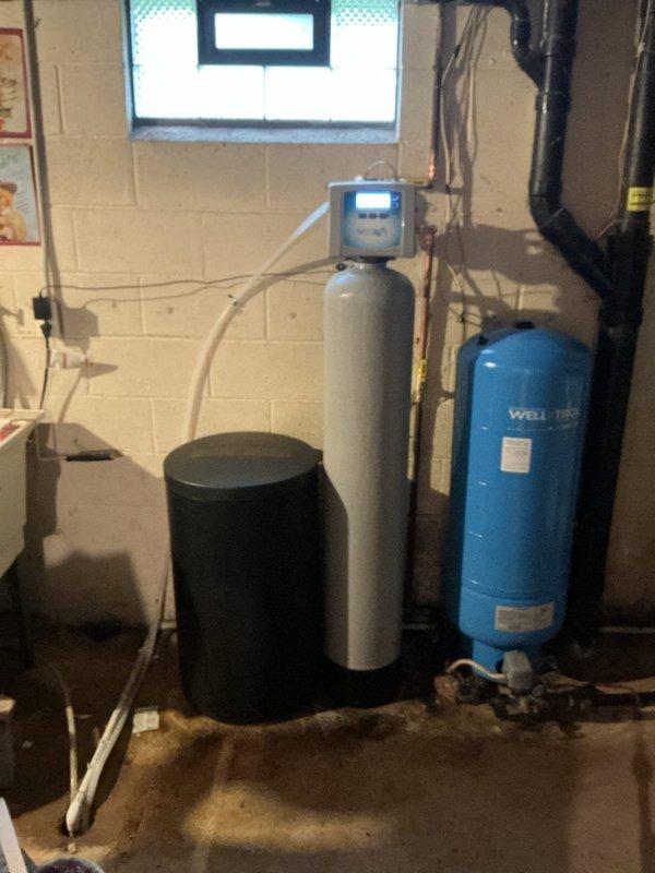 Removed and replaced existing water softener system with new sanitizer softener unit. Tied new system into incoming water supply line at location of previous unit and connected discharge line to existing floor drain. Installed digital control head on softener tank, completed all necessary piping connections using copper and PVC, and integrated system with existing well pressure tank. Delivered and staged six bags of salt for system startup. Tested all connections for proper operation and verified system functionality.