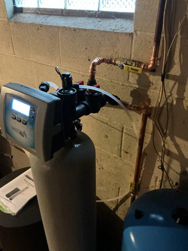 Removed and replaced existing water softener system with new sanitizer softener unit. Tied new system into incoming water supply line at location of previous unit and connected discharge line to existing floor drain. Installed digital control head on softener tank, completed all necessary piping connections using copper and PVC, and integrated system with existing well pressure tank. Delivered and staged six bags of salt for system startup. Tested all connections for proper operation and verified system functionality.