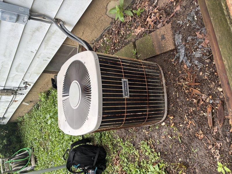 # No Cool Service Call - 20-Year-Old Carrier AC Unit

Responded to a no cooling complaint on an approximately 20-year-old Carrier air conditioning system. Upon arrival, performed visual inspection of the outdoor condensing unit. Found the condenser coils heavily soiled with accumulated dirt, debris, and organic matter, significantly restricting airflow through the coil surfaces. The unit's cylindrical protective cage showed substantial weathering and the surrounding area contained leaves, mulch, and vegetation debris contributing to reduced system efficiency.

Documented equipment condition through photographs showing deteriorated component surfaces, staining on the unit's base panel, and environmental wear consistent with two decades of outdoor exposure. The condenser's placement on bare ground with inadequate clearance from surrounding vegetation and debris contributed to accelerated dirt accumulation on critical heat exchange surfaces.

Given the system's age at 20 years and the ext