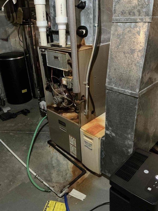 Conducted comprehensive HVAC system evaluation in residential basement mechanical room. Inspected existing furnace unit showing visible corrosion and rust discoloration on burner assembly and internal components. Documented current system configuration including PVC venting, drainage systems, and galvanized ductwork displaying age-related wear and dust accumulation. Photographed equipment condition to support replacement estimate recommendations for aging HVAC system.