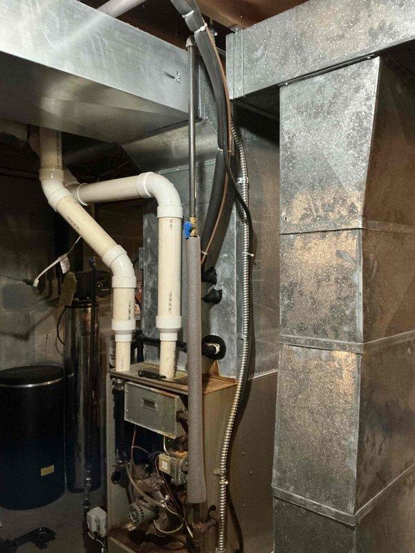 Conducted comprehensive HVAC system evaluation in residential basement mechanical room. Inspected existing furnace unit showing visible corrosion and rust discoloration on burner assembly and internal components. Documented current system configuration including PVC venting, drainage systems, and galvanized ductwork displaying age-related wear and dust accumulation. Photographed equipment condition to support replacement estimate recommendations for aging HVAC system.