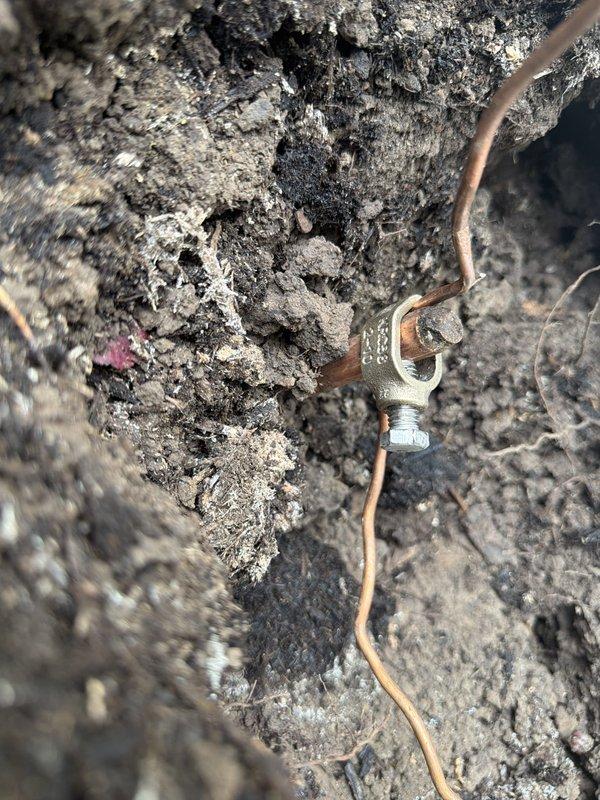 Responded to failed electrical inspection for grounding system deficiencies. Upon arrival, located two ground rods marked with identification flags in landscaped area. Inspection revealed ground rod clamp at first ground rod was not properly attached to the ground rod itself, compromising the grounding electrode system integrity. Additionally, found the grounding electrode conductor (GEC) wire exhibited significant damage at both ground rod connection points, with visible deterioration and compromised insulation. Documented all deficiencies with photographs showing the disconnected clamp, damaged conductor, and overall condition of the grounding system components. Work completed in one hour.