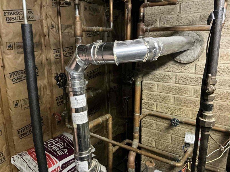 Performed estimate for 47-year-old boiler system experiencing no heat and no hot water production. Unit is a standard boiler, not a combination system. Assessed existing mechanical room infrastructure including aged copper piping, electrical panels, and venting configuration. Documented current system condition with photos showing metallic flue pipe installation, exposed utility connections, and overall mechanical room layout. Provided quote for new boiler replacement with updated venting system to restore heating and domestic hot water functionality.