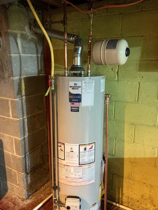 Installed a new 40-gallon Bradford White residential water heater in basement utility area. Installation included connecting copper hot and cold water supply lines with proper fittings, installing ball valve for water shut-off control, mounting white expansion tank to wall, and connecting yellow flexible gas line with emergency shut-off valve. All connections were properly soldered and secured, with pressure relief valve and discharge piping installed per code requirements.