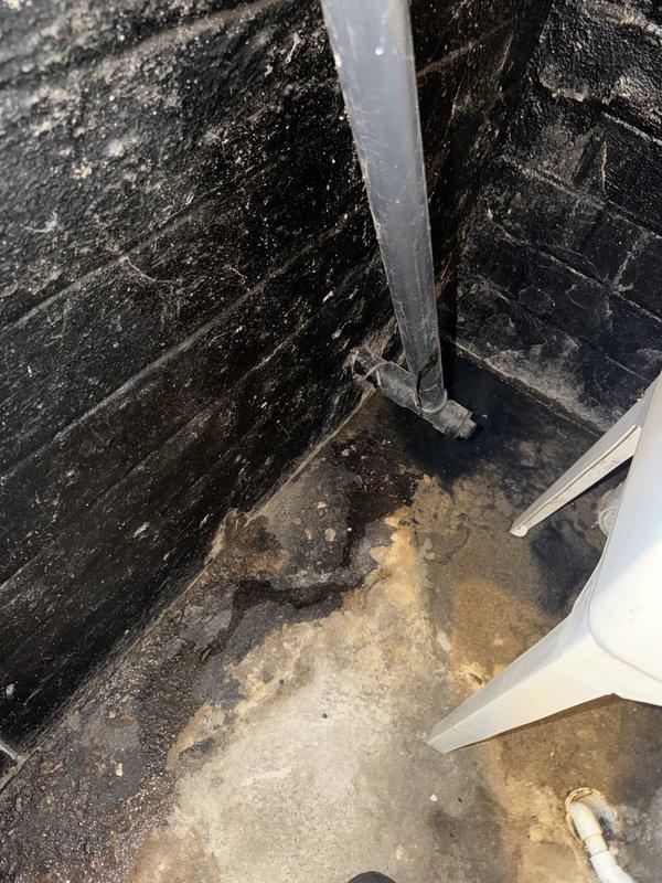 Responded to water leak emergency in basement area. Upon arrival, identified active water intrusion through wall where vertical pipe penetrates from upper level into basement space. Inspected affected area and documented extensive water damage to basement walls and flooring, including significant moisture deterioration, staining, and mold growth in corner section. Traced leak source to compromised pipe connection or breach in vertical plumbing line running through wall cavity. Assessed damage to surrounding building materials including deteriorated wall surfaces and water-stained concrete floor. Photographed conditions showing severity of water infiltration and structural impact to basement interior. Provided diagnostic evaluation and recommendations for repair of leaking pipe and necessary remediation of water-damaged surfaces.