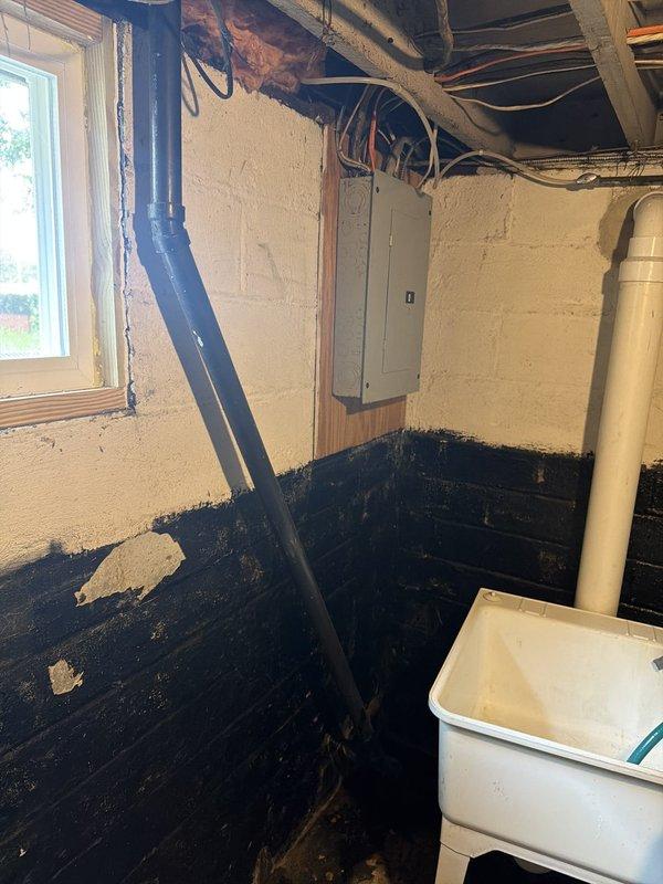 Responded to water leak emergency in basement area. Upon arrival, identified active water intrusion through wall where vertical pipe penetrates from upper level into basement space. Inspected affected area and documented extensive water damage to basement walls and flooring, including significant moisture deterioration, staining, and mold growth in corner section. Traced leak source to compromised pipe connection or breach in vertical plumbing line running through wall cavity. Assessed damage to surrounding building materials including deteriorated wall surfaces and water-stained concrete floor. Photographed conditions showing severity of water infiltration and structural impact to basement interior. Provided diagnostic evaluation and recommendations for repair of leaking pipe and necessary remediation of water-damaged surfaces.
