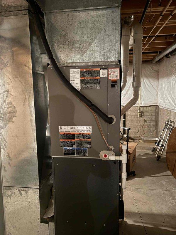 Completed installation of new residential air conditioning system including outdoor condensing unit and indoor evaporator coil. The outdoor unit was properly positioned on a gravel pad against the building exterior with refrigerant lines connected to the indoor coil mounted above the existing furnace in the basement mechanical room. System was installed per manufacturer specifications, refrigerant lines were insulated and secured, electrical connections were completed at the outdoor disconnect, and the unit was tested to verify proper operation and cooling performance.