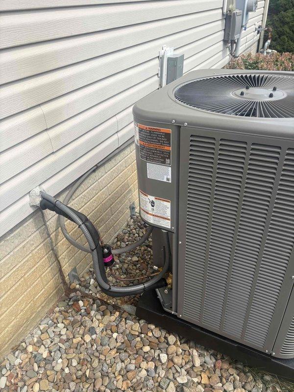Completed installation of new residential air conditioning system including outdoor condensing unit and indoor evaporator coil. The outdoor unit was properly positioned on a gravel pad against the building exterior with refrigerant lines connected to the indoor coil mounted above the existing furnace in the basement mechanical room. System was installed per manufacturer specifications, refrigerant lines were insulated and secured, electrical connections were completed at the outdoor disconnect, and the unit was tested to verify proper operation and cooling performance.