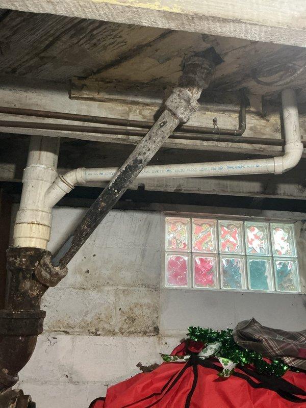 Responded to water leak in downpipe from first-floor toilet in 110-year-old home with newer bathroom addition. Accessed PVC drainage system from basement to locate and identify leak source in vertical drain stack. Inspected toilet connections, floor flange, and waste pipe joints in bathroom above, then traced piping through floor joists to pinpoint leak at compromised fitting connection in basement ceiling area. Tightened loose joint connection and verified proper seal on PVC drainage assembly. Tested system by flushing toilet multiple times and running water to confirm leak was resolved with no further dripping or moisture accumulation. Documented existing conditions of basement plumbing infrastructure and bathroom installation with photographs for reference.