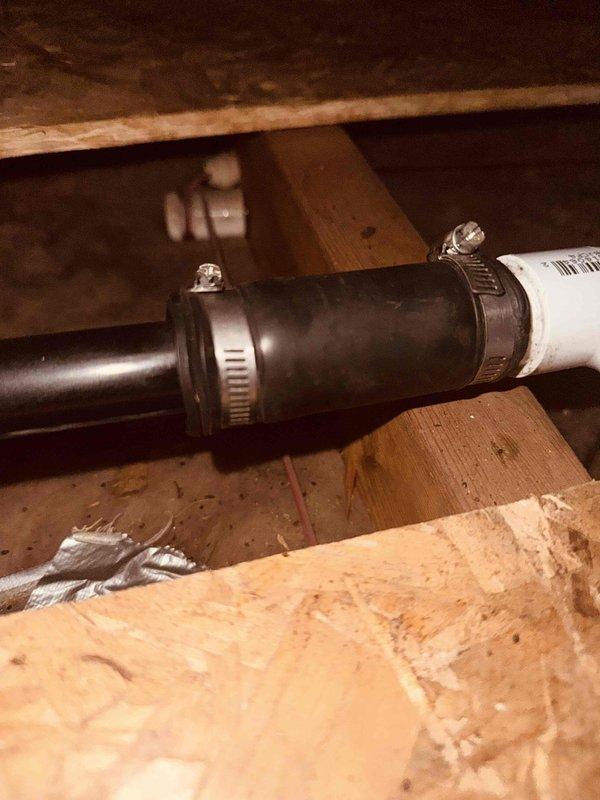 Installed rubber coupling bushings on HVAC condensate drain lines in attic space to reduce vibration and prevent noise transmission through piping system. Connected black drain pipes to white PVC drainage system using flexible Fernco-style rubber couplings secured with stainless steel hose clamps, ensuring proper alignment and watertight seals at all connection points.