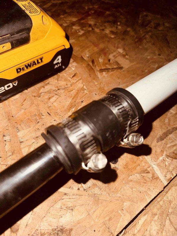 Installed rubber coupling bushings on HVAC condensate drain lines in attic space to reduce vibration and prevent noise transmission through piping system. Connected black drain pipes to white PVC drainage system using flexible Fernco-style rubber couplings secured with stainless steel hose clamps, ensuring proper alignment and watertight seals at all connection points.