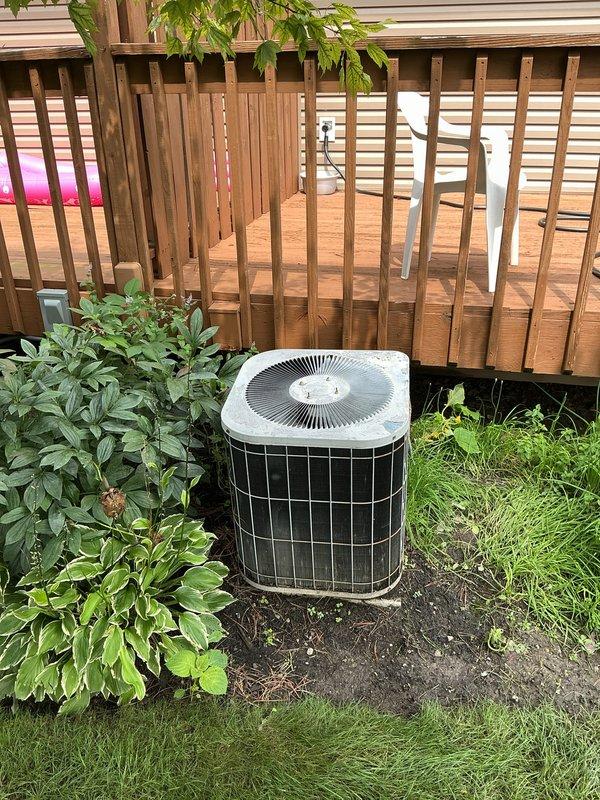 Completed installation of new air conditioning system including outdoor condenser unit and indoor evaporator coil. The outdoor condenser unit was positioned in a landscaped area adjacent to wooden deck structure, ensuring proper clearance and airflow around the equipment. Unit utilizes R-454B refrigerant and was installed on stable ground surface with appropriate drainage considerations. Indoor evaporator coil was installed in utility area with all required safety labels and manufacturer specifications clearly visible. System was properly connected with refrigerant lines and condensate drainage. All electrical connections completed to manufacturer specifications and local code requirements. Equipment tested and verified operational upon completion of installation.