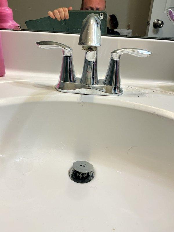 Responded to service call for multiple plumbing issues in residential bathroom. Inspected two 19-year-old toilets: first unit exhibited water leakage from base indicating failed wax ring seal; second unit produced abnormal air horn noise during fill cycle suggesting faulty fill valve or ballcock assembly. Additionally assessed bathroom sink faucet with active leak, likely caused by deteriorated internal seals or cartridge failure. Documented all fixtures with photographs including chrome two-handle centerset faucet assembly and supply line connections for repair recommendations and future service reference.