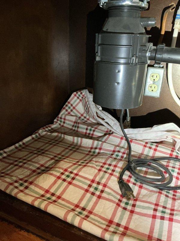 Responded to report of water leak under kitchen sink with concern about loose spigot or malfunctioning garbage disposal. Upon inspection, identified active leak originating from garbage disposal unit and discharge connections. Assessed mounting hardware, drain connections, and disposal discharge pipe for proper seal and alignment. Placed absorbent materials beneath unit to contain water damage during diagnostic evaluation. Inspected water heater components in adjacent area as part of comprehensive plumbing system assessment. Verified all connections, tightened mounting assemblies, and tested for proper drainage flow to resolve leak issue.