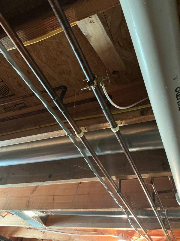 Responded to water leak from copper refrigerator supply line in basement. Upon inspection, located the compromised copper water line running through the exposed ceiling joists. Assessed the existing plumbing configuration, including multiple copper pipe runs secured with mounting brackets throughout the unfinished ceiling space. Identified the source of the leak and performed necessary repairs to restore proper water flow to the refrigerator while eliminating the active leak. Documented the existing plumbing infrastructure and repair work with photographs for service records.