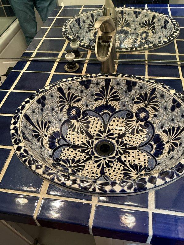 Responded to service call for bathroom sink drainage issue in 50-year-old residential property. Upon arrival, inspected dual vessel sink vanity with decorative Talavera-style basins mounted on tiled countertop. Assessed drainage system and accessed plumbing infrastructure through utility room to identify blockage source. Located obstruction in drain line and cleared clog using appropriate tools and methods. Verified proper water flow and drainage function at affected fixture. Tested system to ensure complete restoration of normal operation. Photographed plumbing infrastructure and completed work for service documentation.