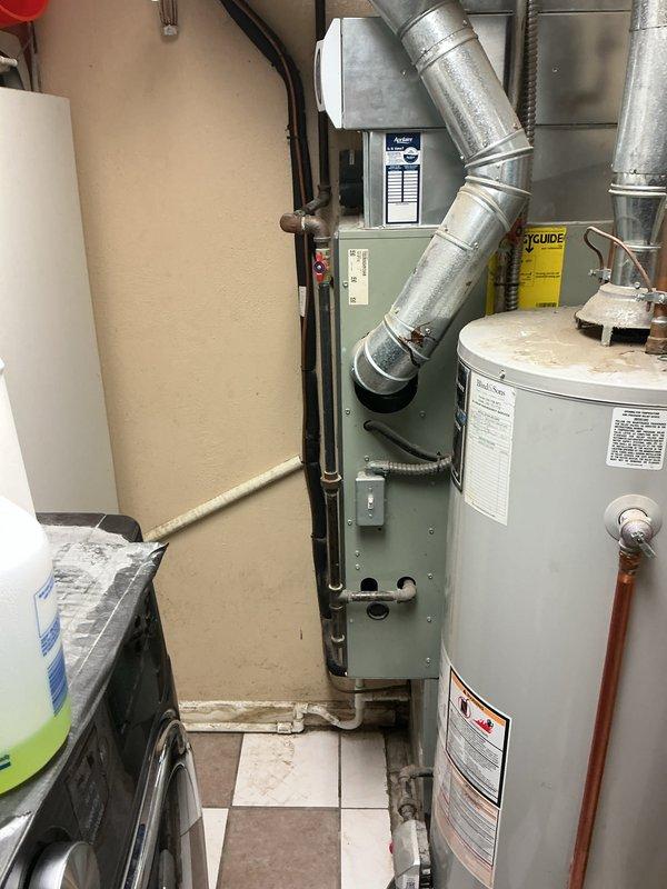 Completed full HVAC system installation including 80% downflow furnace with metal supply ductwork, air conditioning condenser unit, and hot water heater. The Trane AC condenser was positioned on a concrete pad with proper lineset routing and electrical disconnect mounted to exterior siding. Interior mechanical room installation included the downflow furnace with galvanized ductwork transition and new water heater with copper supply connections, all installed per manufacturer specifications and local code requirements.