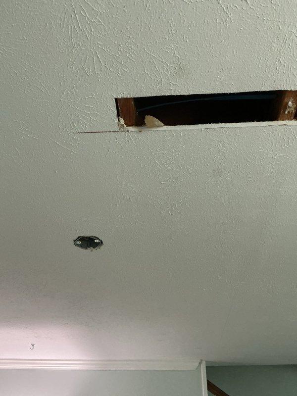 Converted existing three-way switch controlling living room outlet to constant power configuration and installed new ceiling fan circuit. Ran 3-wire switch leg from existing switch location through ceiling to center of room, cutting access through drywall as needed to route wiring. Installed fan-rated junction box at ceiling center for future customer installation of ceiling fan. In two upstairs bathrooms, removed existing outlets and standard boxes, then installed new single-gang old work boxes and wired customer-supplied GFCI receptacles. Made straight cuts in drywall where possible and secured cut pieces back in place where feasible.