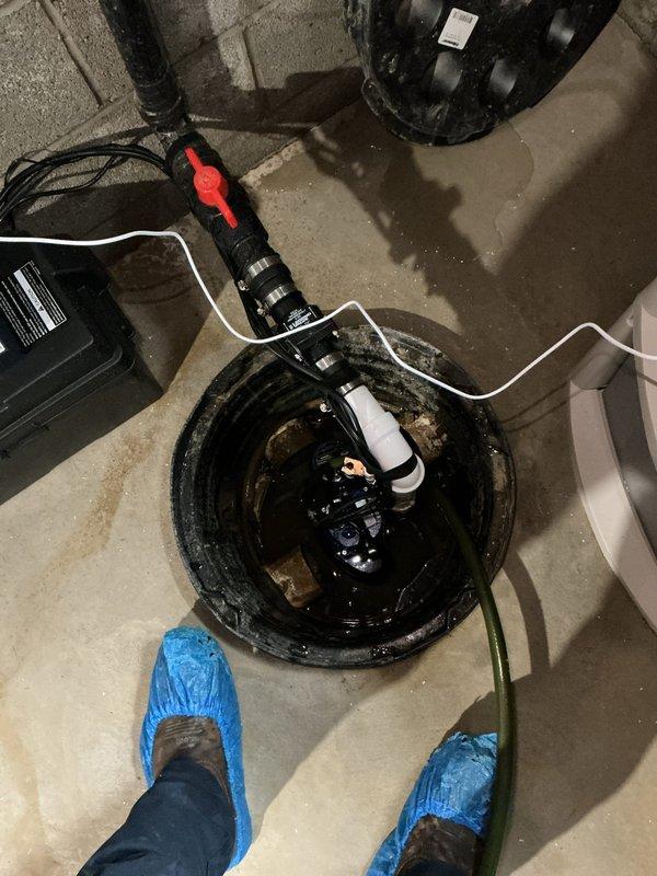Removed existing battery backup system from sump pump installation and replaced with new battery backup unit, including fresh battery and associated piping and fittings. Work involved disconnecting old power cables and alligator clip connections, installing new backup system adjacent to existing sump pump basin, and ensuring proper electrical connections between battery unit and pump mechanism. All necessary pipe modifications and fittings were completed to integrate the new backup system with the existing sump pump configuration for reliable emergency operation during power outages.