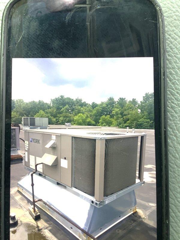 Conducted rooftop commercial HVAC equipment assessment using extension ladder to access single-story roof. Evaluated existing York rooftop unit and additional commercial HVAC equipment for replacement estimate, documenting current conditions with photographs showing unit configuration, weathering patterns, and rooftop membrane condition around equipment bases.