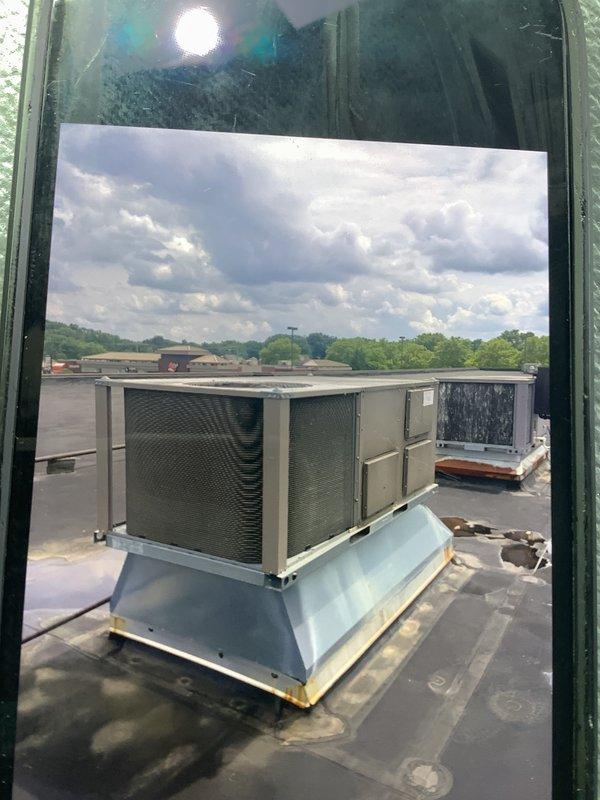 Conducted rooftop commercial HVAC equipment assessment using extension ladder to access single-story roof. Evaluated existing York rooftop unit and additional commercial HVAC equipment for replacement estimate, documenting current conditions with photographs showing unit configuration, weathering patterns, and rooftop membrane condition around equipment bases.
