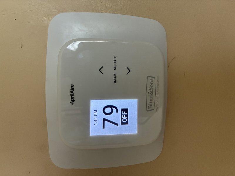 Responded to service call for malfunctioning thermostat. Inspected AprilAire programmable thermostat, removed cover to examine internal wiring and terminal connections. Verified all wire connections at terminal strip were secure, checked system operation, and confirmed thermostat was functioning properly with display reading accurately at 79°F.