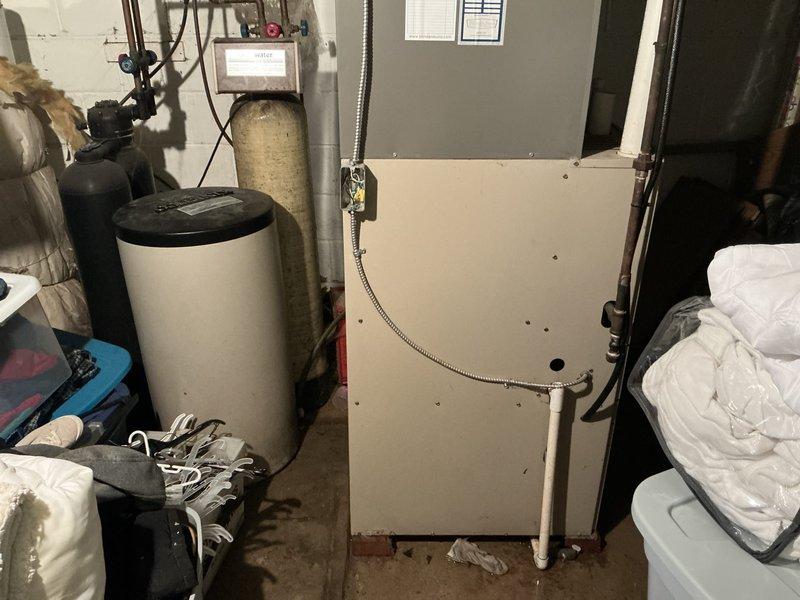 Completed furnace replacement estimate for 18-year-old downflow unit with 120,000 BTU capacity located in basement utility area. Assessed existing HVAC system, documented equipment condition and specifications, photographed installation site including current air handler configuration, surrounding water treatment equipment, and available workspace for replacement unit installation.