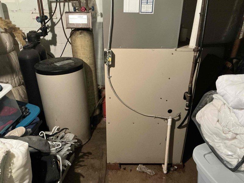 Completed furnace replacement estimate for 18-year-old downflow unit with 120,000 BTU capacity located in basement utility area. Assessed existing HVAC system, documented equipment condition and specifications, photographed installation site including current air handler configuration, surrounding water treatment equipment, and available workspace for replacement unit installation.