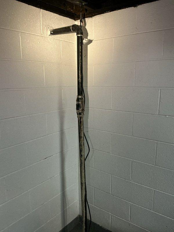 Responded to active water leak in basement originating from drainage system connected to upstairs kitchen sink in 50-year-old residential property. Upon inspection, identified compromised piping at vertical black drain stack where kitchen waste line tied in at ceiling level. Leak was actively dripping along pipe run and required immediate attention to prevent further water damage to basement area. 

Assessed existing plumbing infrastructure, including PVC trap assembly and drain connections beneath kitchen sink. Documented conditions with photographs showing aged black iron stack pipe with visible weathering and deterioration, as well as under-sink plumbing configuration with white PVC fittings and flexible metallic conduit for electrical components. Verified leak source and determined repair requirements for aging drainage system.

Provided estimate for sump pump installation with backup battery system as requested to address basement water management concerns.
