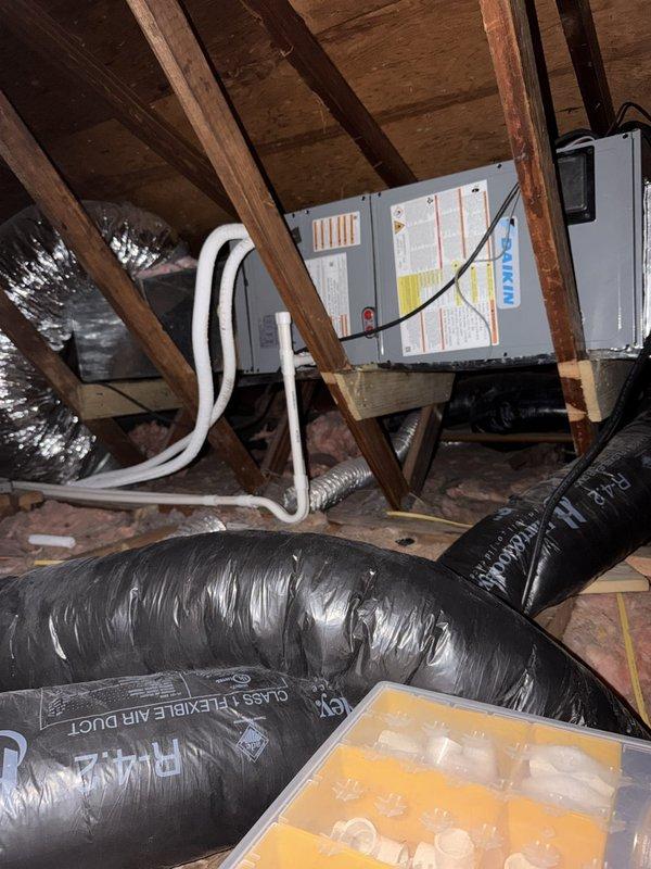 Completed full ductless mini-split system installation including attic-mounted air handler with new ductwork distribution and single indoor wall-mounted head unit. Installed gray metal air handler on platform between attic joists with proper structural support, ran flexible supply and return ductwork throughout attic space with appropriate insulation, and mounted interior ceiling register with white louver grille for conditioned air distribution. Installed indoor ductless head unit in living space with thermostat control panel for zone temperature management, ensuring proper refrigerant line connections, condensate drainage, and electrical service to both indoor and outdoor components for complete system operation.
