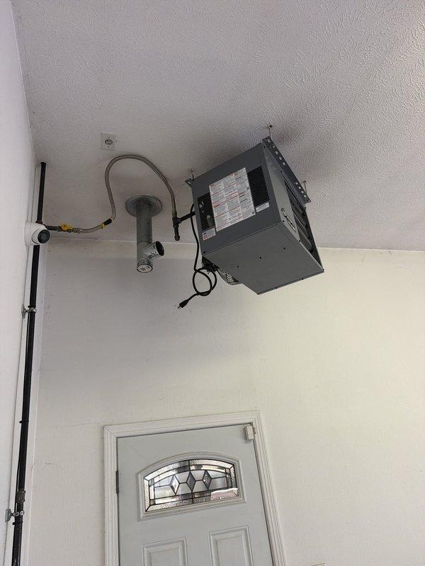 Installed customer-supplied garage heater unit in residential garage space. Mounted gray metal heating unit to upper wall corner near ceiling with secure mounting brackets, ran black electrical conduit vertically down wall for power supply, and completed all electrical connections to ensure proper operation of the wall-mounted heating system.