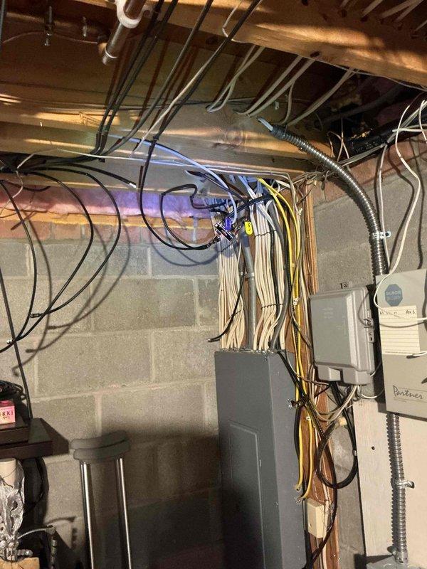 Completed on-site electrical estimate for standby generator installation in unfinished basement utility area. Assessed existing electrical infrastructure including main service panel, conduit routing pathways, and available space for generator transfer switch installation. Documented current electrical configuration with multiple branch circuits, PVC and metal conduit runs along ceiling joists, and concrete block foundation walls suitable for equipment mounting. Photographed utility room layout showing HVAC ductwork, plumbing systems, and electrical panel to determine optimal placement for automatic transfer switch and feeder conductors from future generator location.